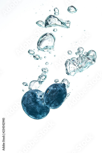 Two blueberry’s splashing into crystal clear water with air bubbles