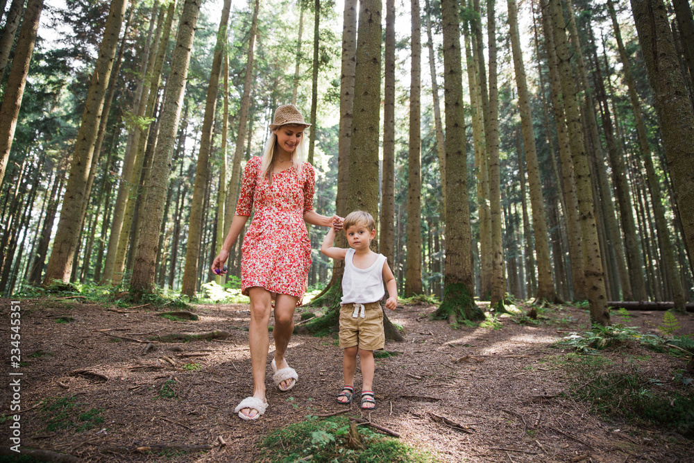 Happy young mother walking with her cute little son in the forest