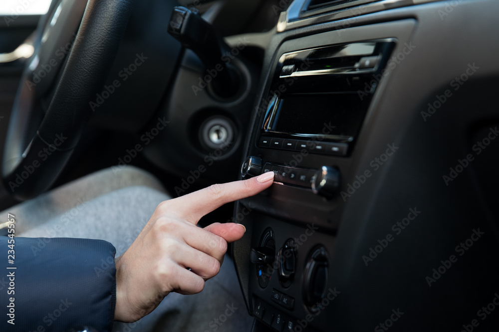 A girl in a winter jacket sitting on the driver's seat in the car and presses the button