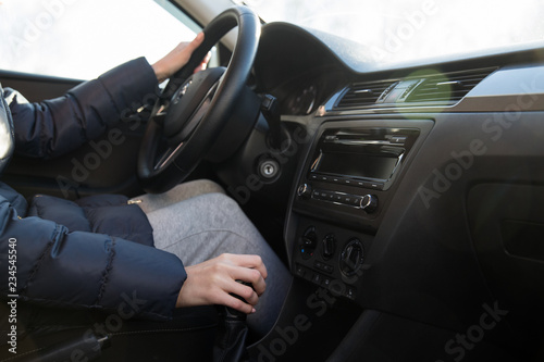 A girl in a winter jacket drives a car and switches gears