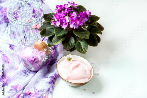 spa setting with cosmetic cream, bath salt and African violet in flower pot on white wooden table background. Selective focus
