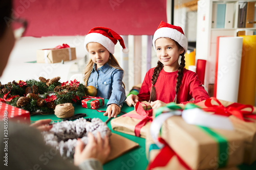 Two little girls in Santa caps preparing gifts for Christmas with their mother
