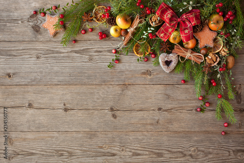 Christmas wooden background with fir branches, apples, cookies, cranberries, nuts and a ribbon bow