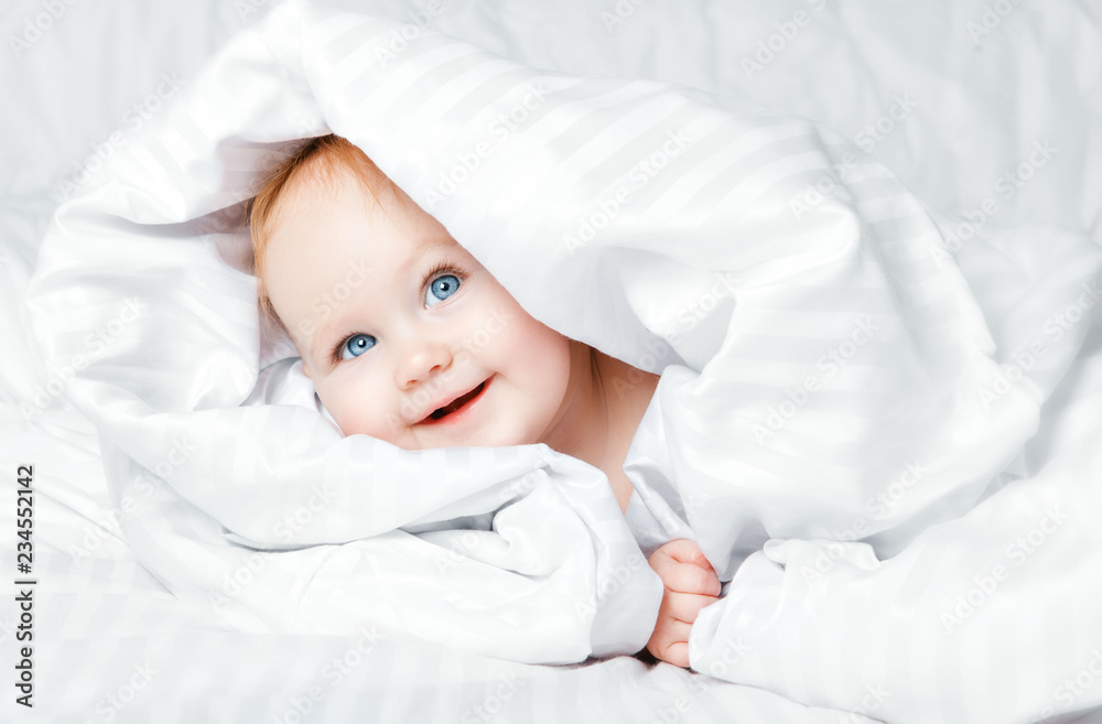 Cute and Happy child with blue eyes looking out of the white blanket. Copy space. Cute and Happy child with blue eyes looking out of the white blanket. Copy space.