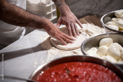 Preparing Pizza dought on a marble countertops. Tomato sauce and mozzarella in the foregound.