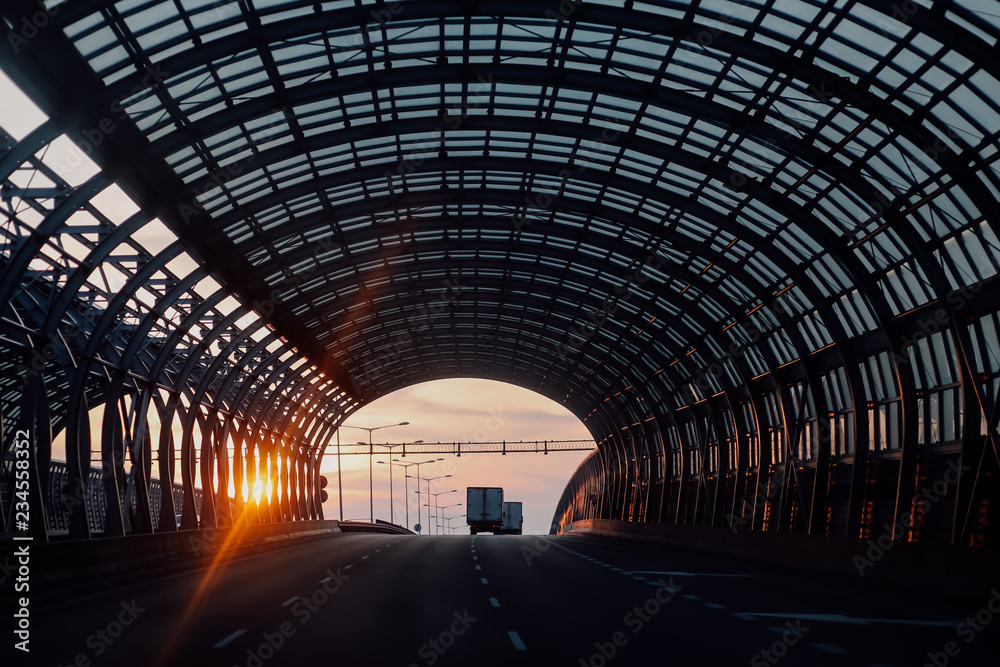 Early morning sunrise at the beautiful modern sound absorbing tunnel of Warsaw. Metal structure and glass. Cars on the highway going to horizon