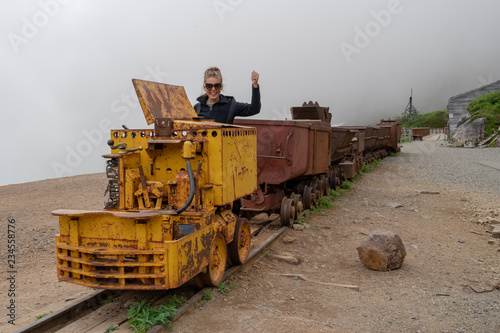 Woman poses as a train conductor on a mining cart at Independence Mine Alaska at Hatcher Pass on a misty foggy day