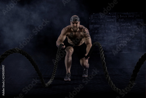 Muscular man working out with battle ropes