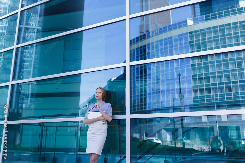 Portrait of business woman with laptop in her hands standing next to the office building.