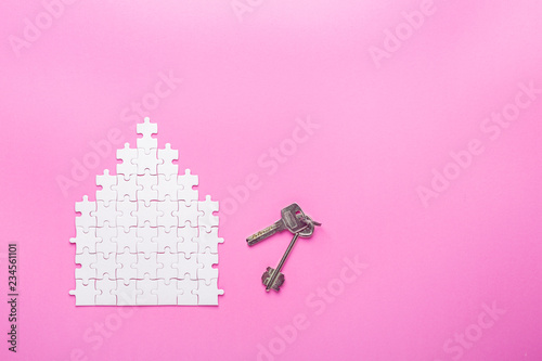 White puzzle. House shape puzzle and key. The concept of rent, mortgage. Pink background. Top view photo