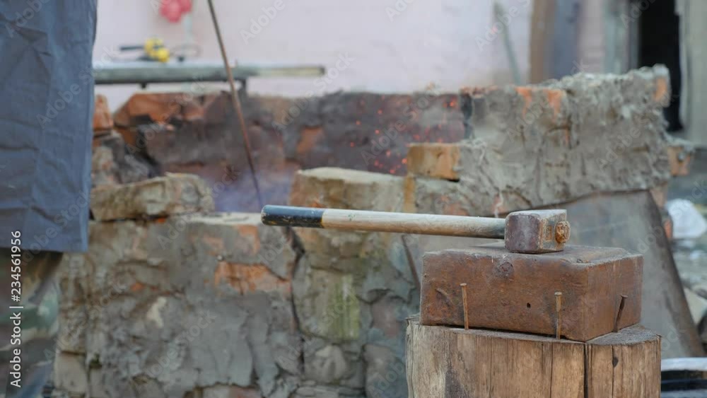 blacksmith works metal. Craftsman, the Highlander on private smithy in the village. sledgehammer lies on the anvil. Master interferes with charcoal in a hot furnace, crucible. blacksmith works metal. Craftsman, the Highlander on private smithy in the village. sledgehammer lies on the anvil. Master interferes with charcoal in a hot furnace, crucible.