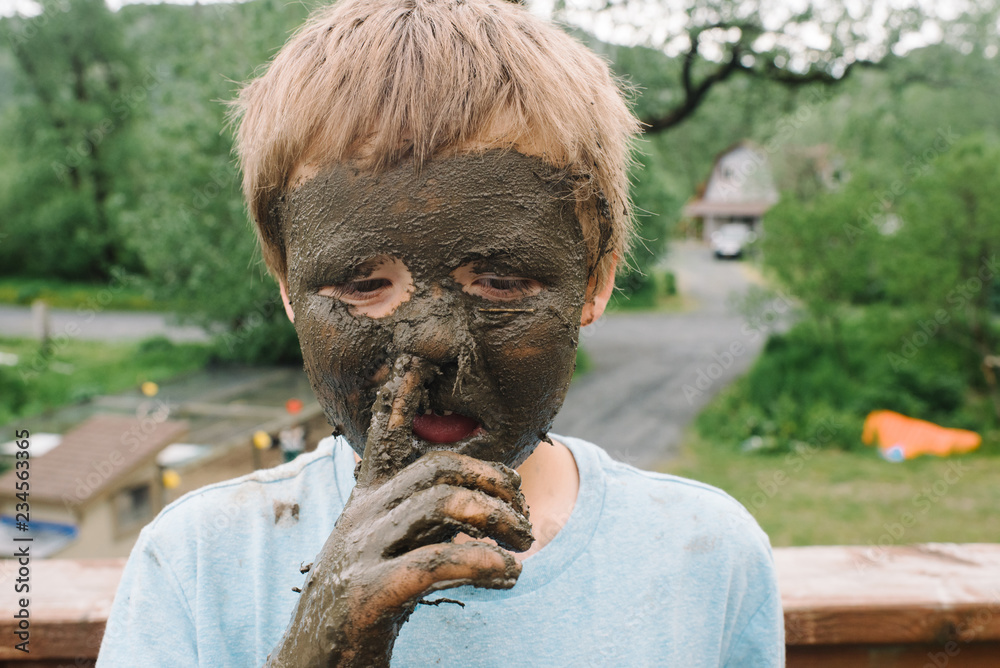 Young boy with mud on his face sticking his finger in his nose Stock