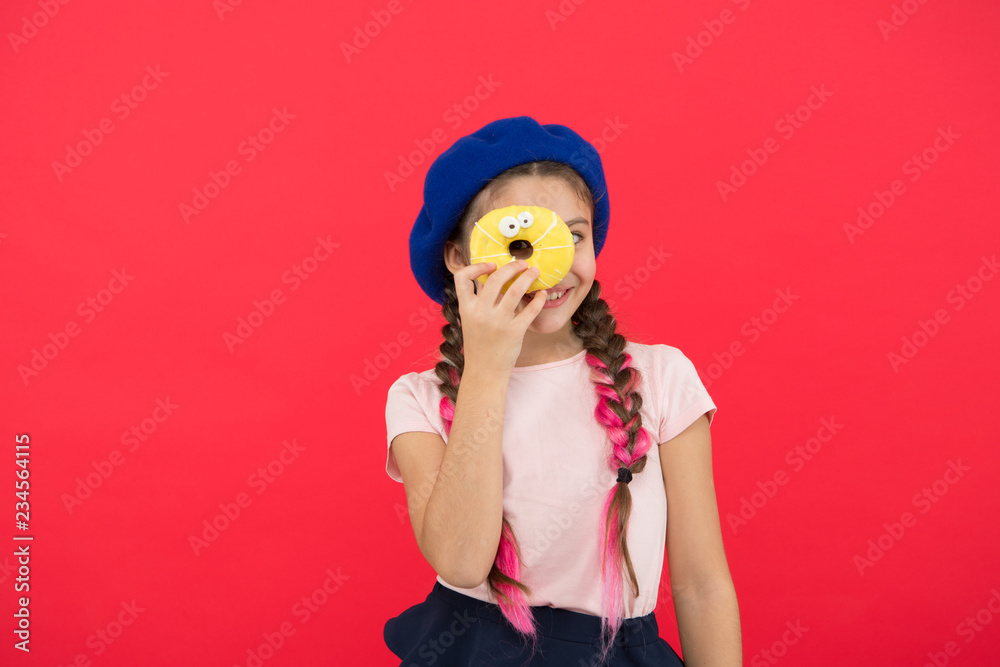 Kid fan of baked donuts. Delicious sweet donut. Girl in beret hat hold donut red background. Kid playful girl eat donut. Health and nutrition concept. Sweet life. Sweets shop and bakery concept