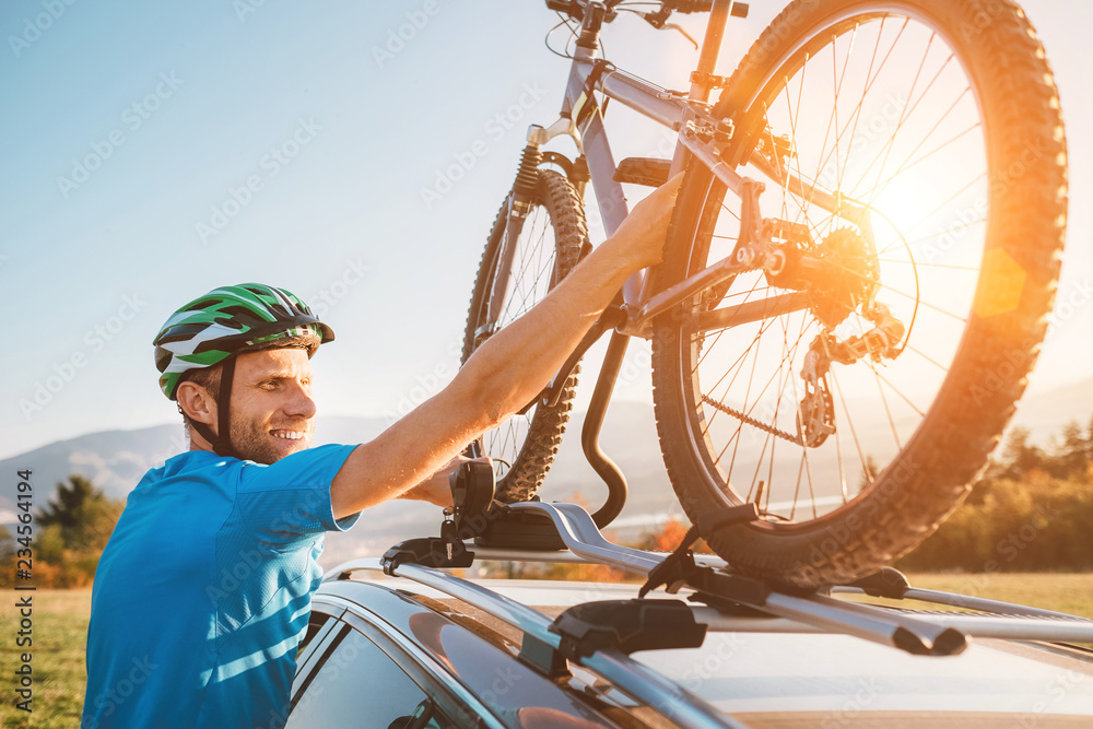 Obraz premium Young Man veared in cycling clothes and protective helmet instals his mountain bike on the car roof