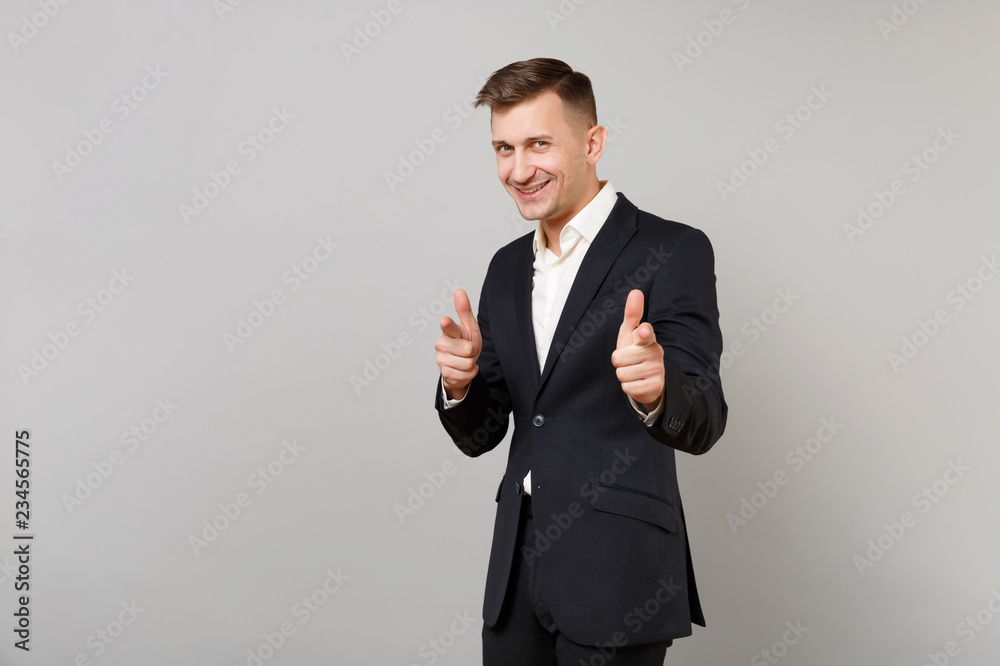 Handsome young business man in classic black suit and shirt pointing index fingers on camera isolated on grey wall background in studio. Achievement career wealth business concept. Mock up copy space. Handsome young business man in classic black suit and shirt pointing index fingers on camera isolated on grey wall background in studio. Achievement career wealth business concept. Mock up copy space.