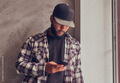 African-American bearded man chatting in the social network while standing next gray textured wall. photo