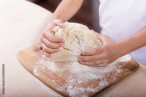 Children's hands knead the dough on a wooden cutting board. close-up. dough recipe, cooking technology
