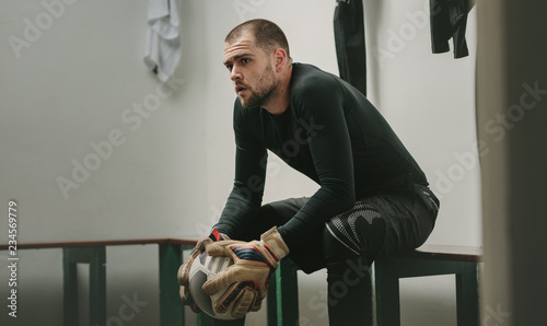 Obraz na plátně Footballer sitting in dressing room holding a football