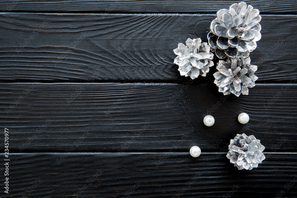 Obraz premium Silver pine cones and a heap of white beads on black wooden table. Free space for text.