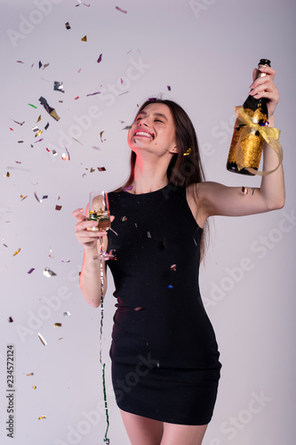 Young and happy girl with tinsel confetti in hands bottle of champange and glass with champagne. New year's feeling. © Vita
