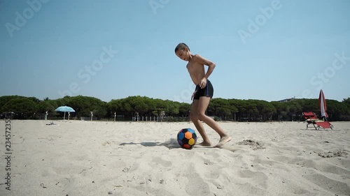 Young boy at the beach plays with a soccer, football ball, SLOW MOTIION photo