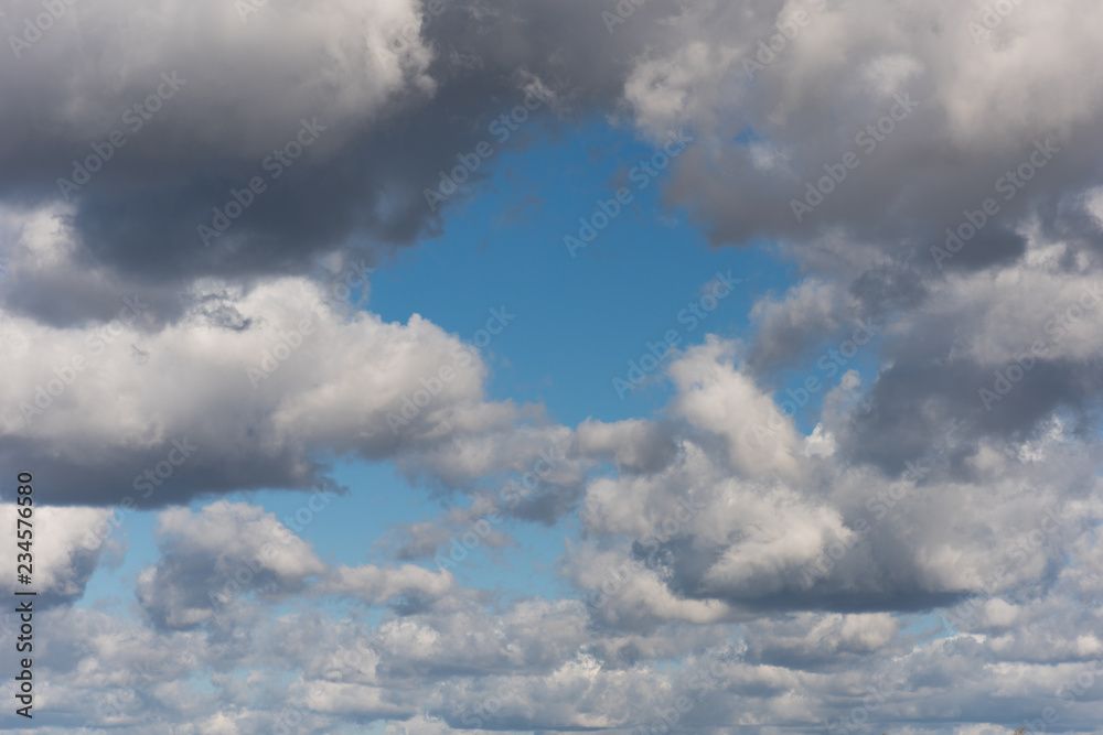 Obraz premium Beautiful white and grey fluffy clouds soar over a deep blue background. Cloudscape with autumn dark storm clouds moving fast over blue sky day.