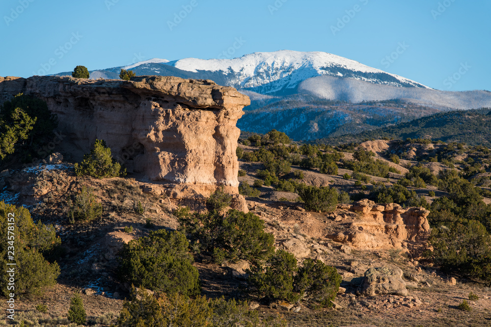 Obraz premium Czerwona formacja skalna z piaskowca z ośnieżonymi szczytami pasma górskiego Sangre de Cristo w oddali w pobliżu Santa Fe w Nowym Meksyku