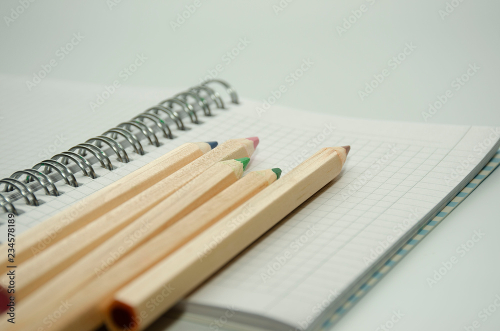Five colored wooden pencils on the background of a blank sheet of notepad on a spring Five colored wooden pencils on the background of a blank sheet of notepad on a spring