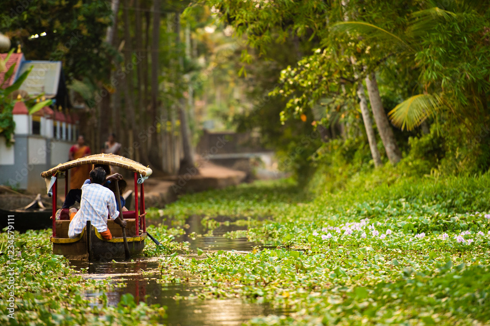 Some tourists are on a canoe sailing on the lush and green backwaters in Alleppey during the sunset, Kerala, India. Alleppey is one of the famous backwater tour destinations in Kerala.
