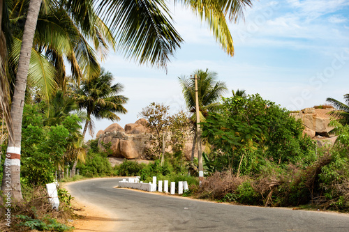 A beautiful narrow road surrounded by lush plants and granite mountains in Hampi, Karnataka, India.
