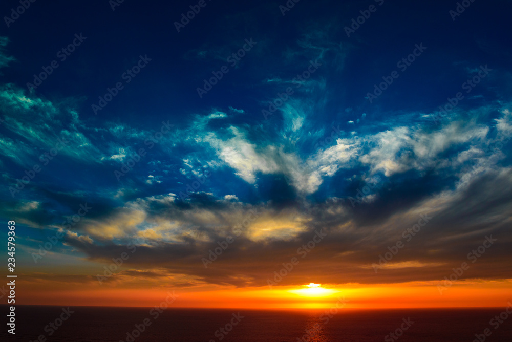 sun setting over a sea horizon behind dramatic cloudscape