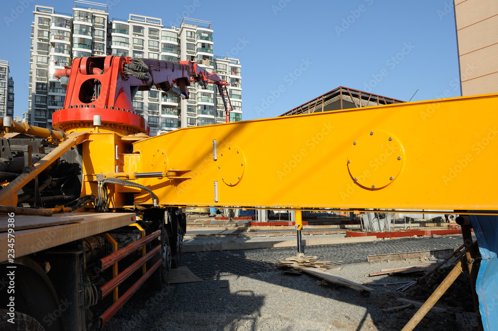 Unusual angle, close-up view at concrete pump truck with yellow arm over construction site in China. residential building in background.
