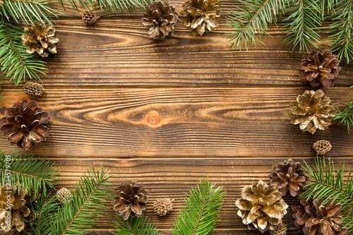 Pine golden cones and fir tree branches branches on brown wooden background. Free space for text. Christmas mood background.