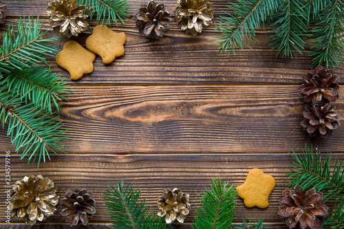 Bell shape gingerbread cookies and frame of golden cones and fir tree branches on brown wooden table. Space for text.