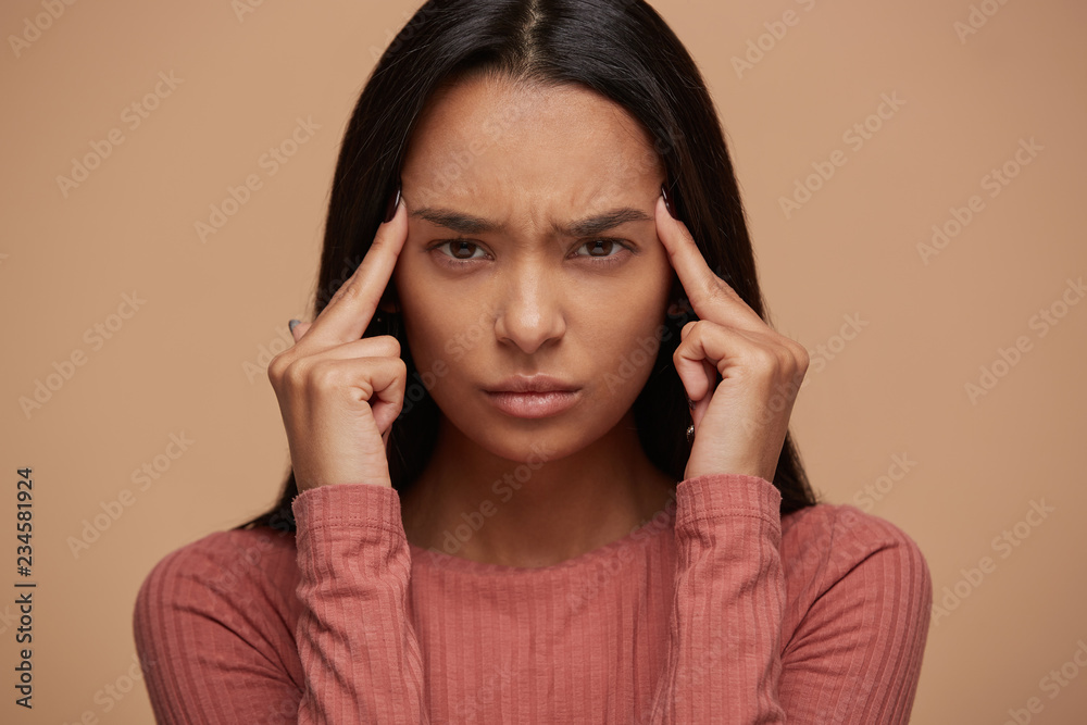 Portrait of upset young asian woman suffering from stress and headache.Young caucasian girl over beige background looks tired, nervous, feels hurt, painful expression on face, negative emotion Portrait of upset young asian woman suffering from stress and headache.Young caucasian girl over beige background looks tired, nervous, feels hurt, painful expression on face, negative emotion