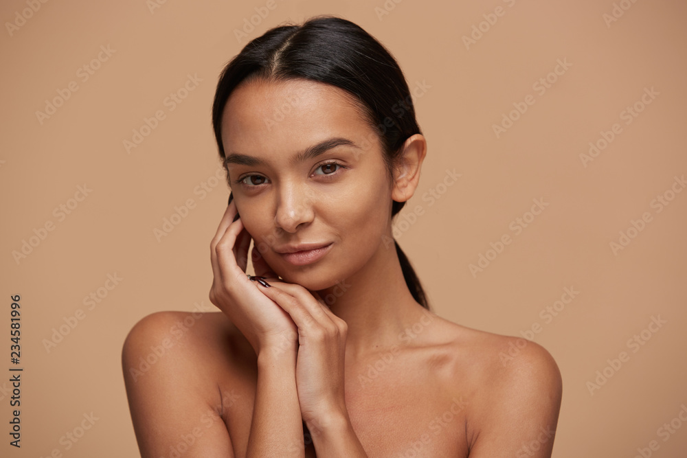 Bliver til Skeptisk essens Head shot of an attractive mixed race girl, looking gently and tenderly,  demonstrates healthy beautiful skin, calm and pleased, keeps hands near the  face, over beige background Stock Photo | Adobe Stock