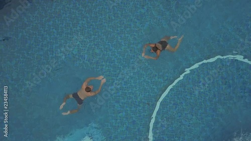 2K Aerial top view of young man and young brunette girl swimming in the thermal water pool in luxury resort. Young couple swim to each other and kiss in the end. Kissing couple