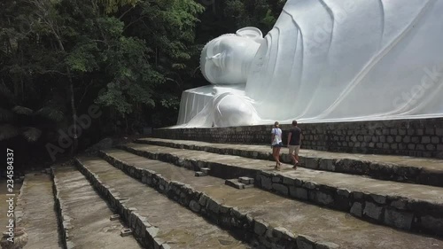 2K Aerial view of two young people walking near big reclining Buddha monument in Ta Cu Mountain, Vietnam 2018. Huge white Big Buddha in Vietnam with wide stairs. Historical ancient object. 