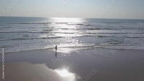 2K Aerial view of young girl in swimsuit walking on the lonely sandy beach from the ocean at sunrise