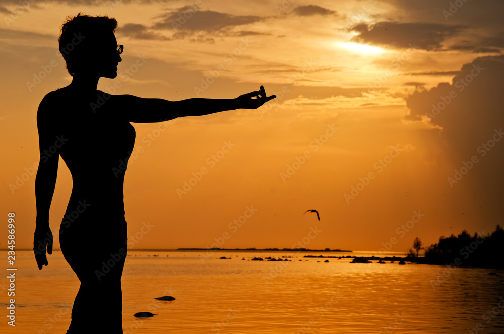 silhouette of a woman stretching her hand to sunset-an evening walk along the summer shore