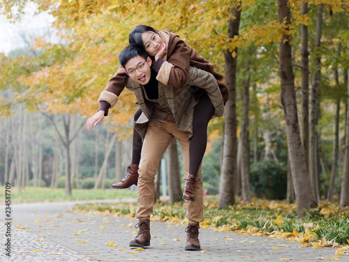 Portrait of smiling young girlfriend piggyback boyfriend during romantic walk in autumn park alley, excited couple looking at camera have fun outdoors, playing foolish, man carry lover on his back.