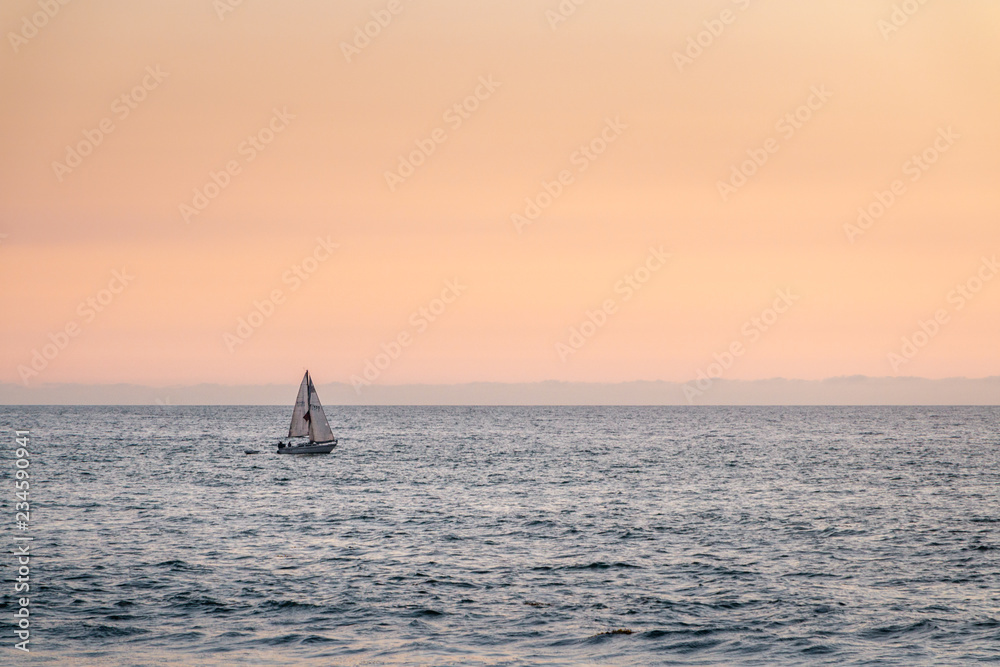 Single sail boat sailing on sea during an orange sunset