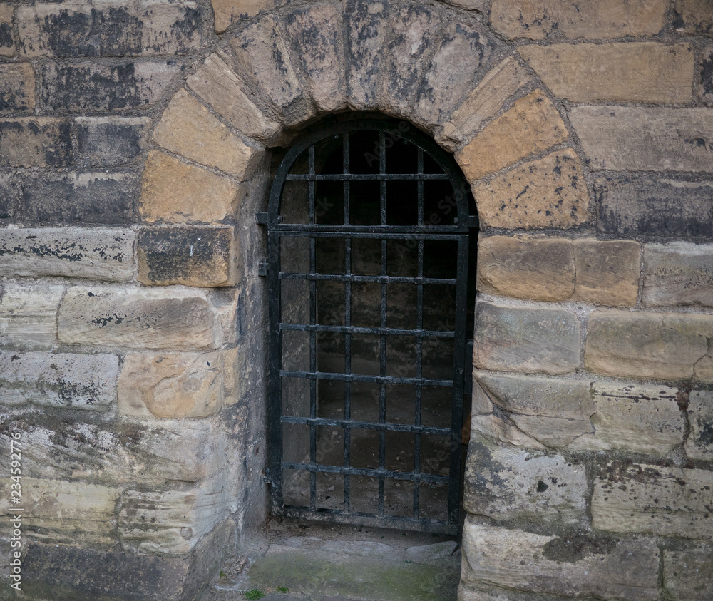 Arched entrance to an old. medieval, stone castle dungeon with iron bars