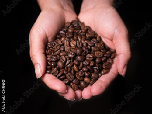 Hands holding fresh roasted natural coffee beans top view from above with black background.