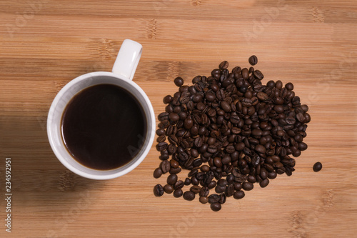 Cup of black Coffee next to freshly roasted coffee beans on a natural wooden background.