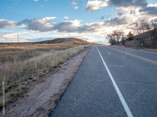 Low Angle View of Country Road Going Up Hill With Tall Dry Grass Fields on the Left © porqueno