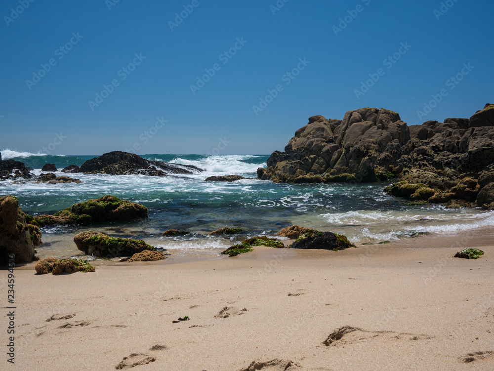 Beautiful sunny beach in Portugal with cloudless blue sky and clear water waves crashing on rocks. Vila do Conde, Porto.