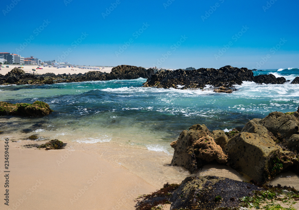 Beautiful sandy beach with rocks on sunny day. Clear blue water and blue cloudless sky in Vila do Conde, Porto, Portugal