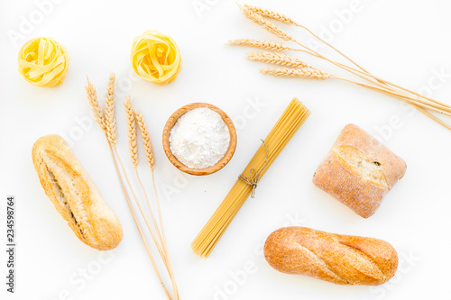 Products made of wheat flour. White flour in bowl, wheat ears, fresh bread and raw pasta on white background top view photo