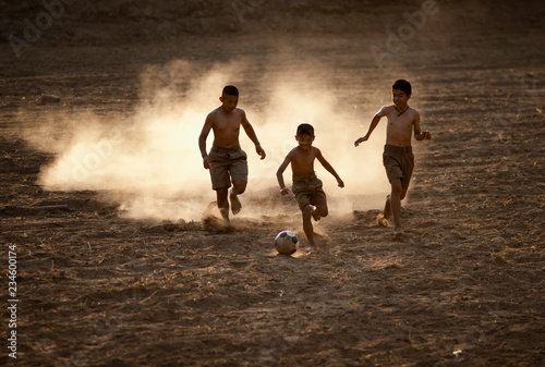 Asian boys friends playing football on the clay ground on summer sunny day. Concept friendship and road to play in the world cup.
